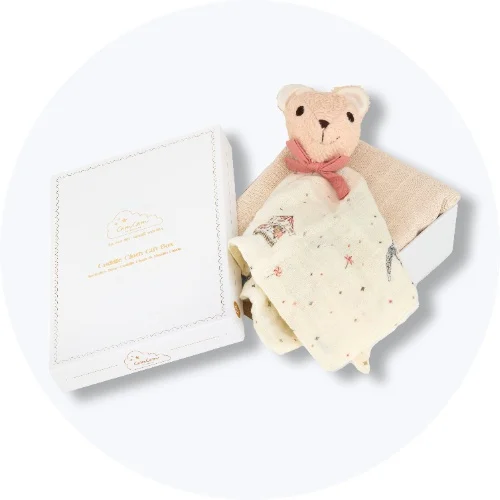 Hvid gaveæske indeholdende en bamseklud med lyserød sløjfe og en cremefarvet stofble med mønster. Tekst: Cuddle Cloth Gift Box.