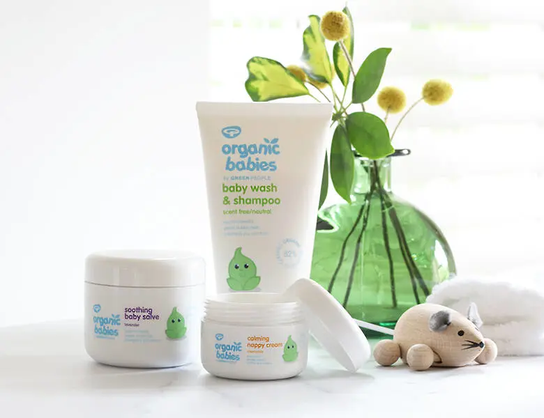 Her ses tre hvide og blå Green People produkter på et hvidt bord med blomster og legetøj på.