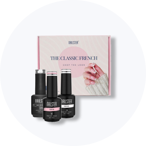 Her ses et billede med en gaveæske fra Nailster placeret mod en lys, rund baggrund. På æsken står teksten “THE CLASSIC FRENCH”. Foran æsken står flere negleprodukter fra Nailster i sort emballage.