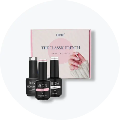 Her ses et billede med en gaveæske fra Nailster placeret mod en lys, rund baggrund. På æsken står teksten “THE CLASSIC FRENCH”. Foran æsken står flere negleprodukter fra Nailster i sort emballage.