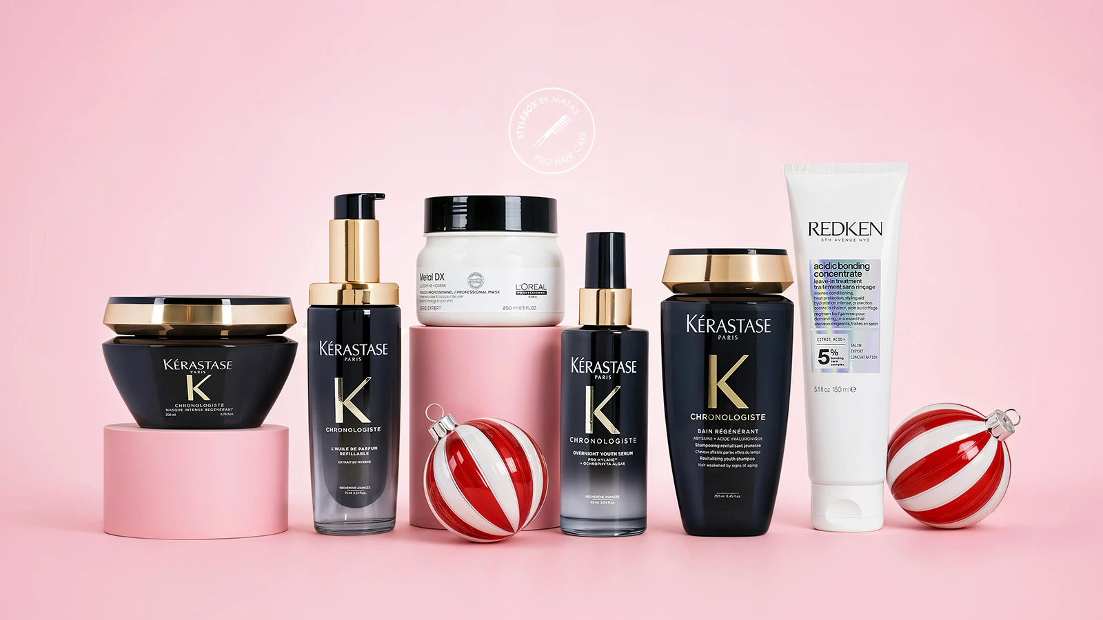 Kérastase Chronologiste, L'Oréal Metal DX og Redken hårplejeprodukter med to julekugler på en lyserød baggrund.
