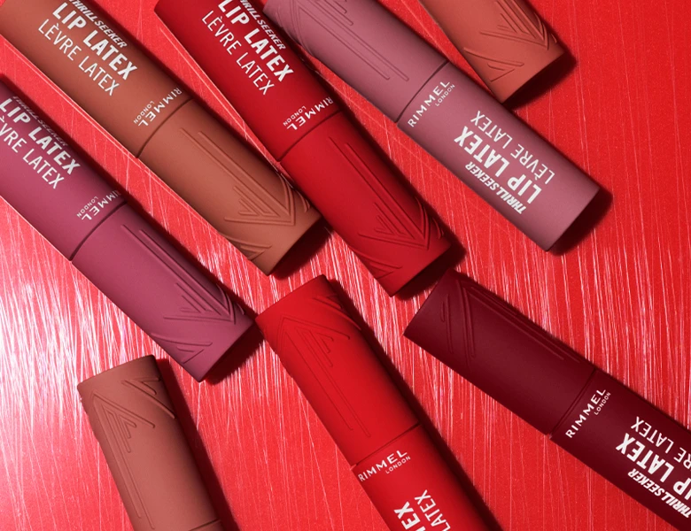 Her ses et billede med flere læbeprodukter fra Rimmel London placeret mod en rød baggrund. På produkterne står teksten “THRILLSEEKER LIP LATEX”, og de er i forskellige røde og nude nuancer.