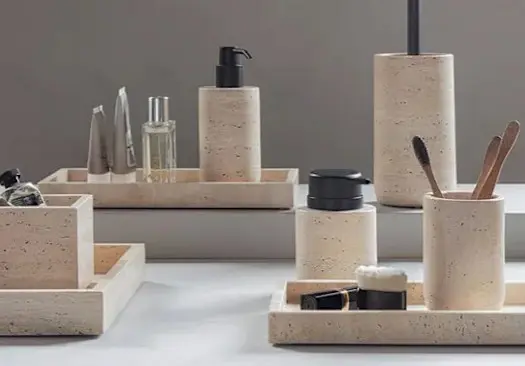 Beige badeværelsestilbehør i steninspireret design med sæbedispenser, tandkrus, bakker og beholdere arrangeret ved et spejl.