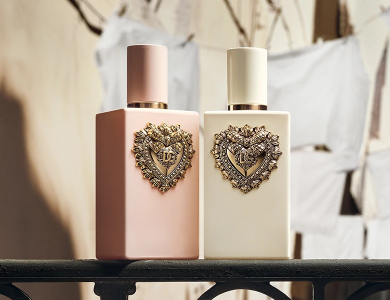 Her ses et kampagnebillede for Dolce & Gabbana Devotion med to personer i sort tøj i en smal gade. Foran dem vises to Devotion-parfumeflakoner i rosa og cremefarvede nuancer. På billedet står “Devotion Dolce & Gabbana” samt “My Devotion and Your Devotion – The New Eau de Parfum Intense”.