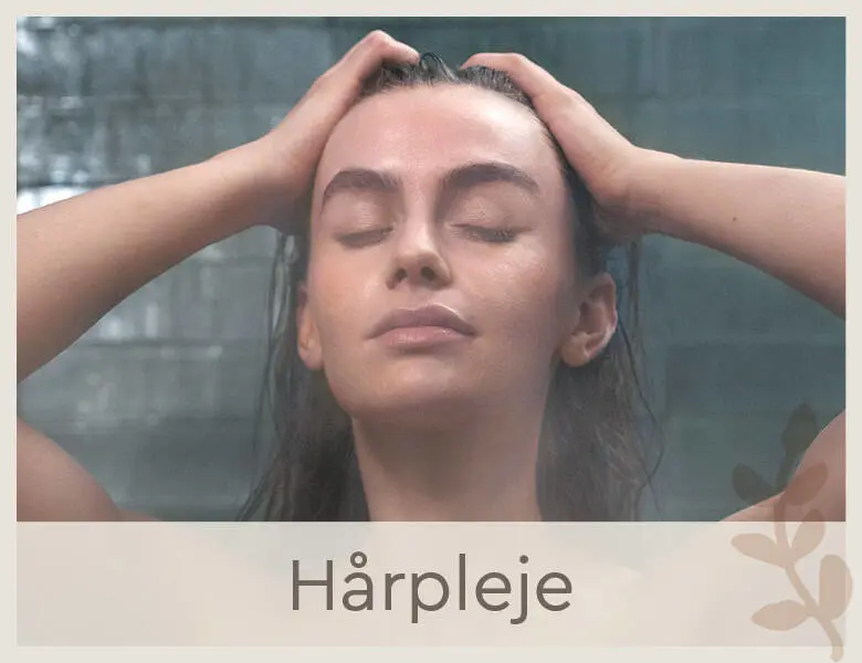 Her ses et billede af en kvindes ansigt. Kvinden står i badet og rører ved sit våde hår. Hun ser afslappet ud.