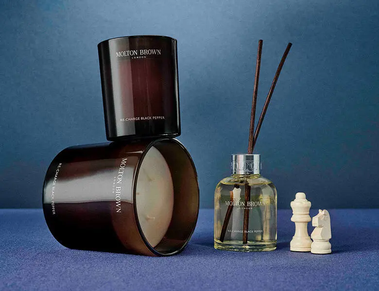 Her ses en blå baggrund med Molton Brown produkter på - disse er duftpinde og duftlys. 