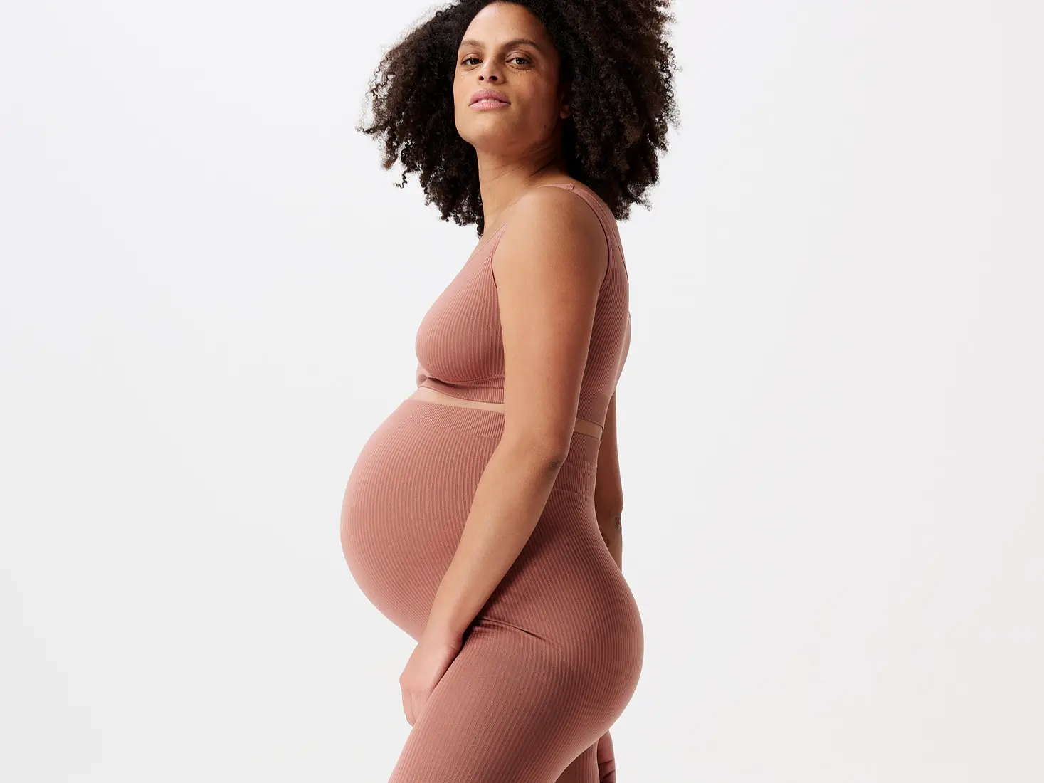 Gravid person i ribbet top og leggings, set fra siden.