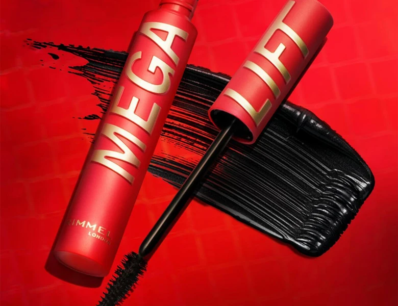 Her ses et billede af en mascara fra Rimmel London placeret mod en rød baggrund med sorte mascarastrøg. På produktet står teksten “MEGA”, og mascaraen vises både lukket og åbnet med synlig børste.