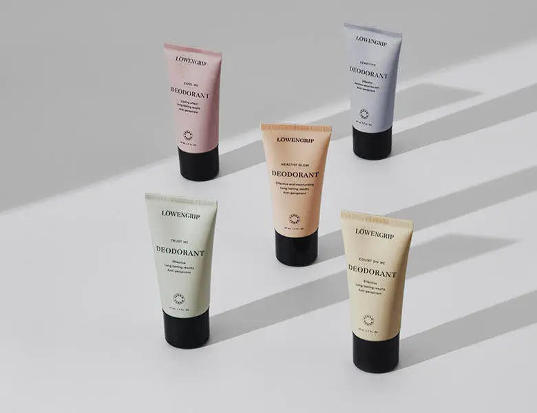 Her ses et billede med fem deodoranter fra Løwengrip placeret på en lys overflade mod en lys baggrund. På produkterne står teksten “DEODORANT”. Produkterne er i forskellige farver som rosa, beige, grøn og grå med sorte låg.