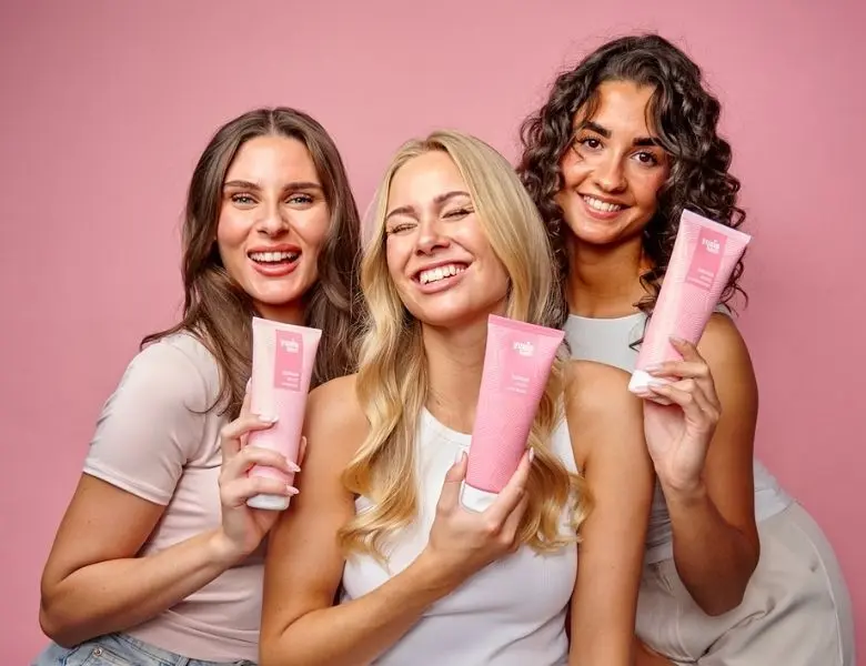 Her ses tre kvinder, der holder Yuaia Hair produkter i pink emballage på en lyserød baggrund.