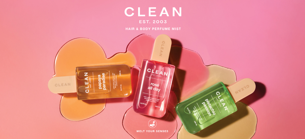 Her ses et billede med tre produkter fra CLEAN placeret mod en lyserød baggrund med farvede væskeformer. Øverst står teksten “CLEAN EST. 2003 HAIR & BODY PERFUME MIST”, og nederst står “MELT YOUR SENSES”. På produkterne står blandt andet “papaya paradise”, “rosé all day” og “pistachio passion”.