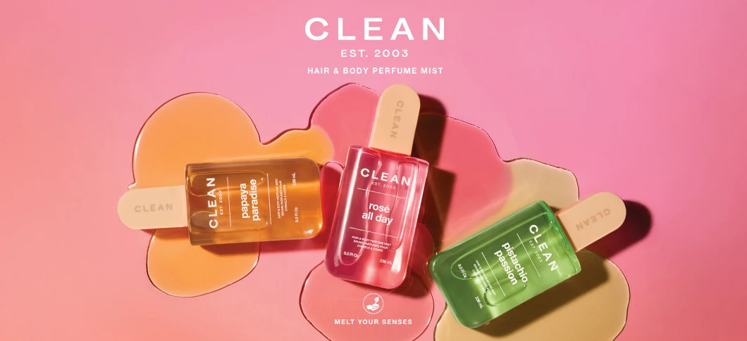 Her ses et billede med tre produkter fra CLEAN placeret mod en lyserød baggrund med farvede væskeformer. Øverst står teksten “CLEAN EST. 2003 HAIR & BODY PERFUME MIST”, og nederst står “MELT YOUR SENSES”. På produkterne står blandt andet “papaya paradise”, “rosé all day” og “pistachio passion”.