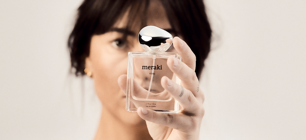 Her ses en person, der holder en Meraki parfume i en glasflaske foran ansigtet.