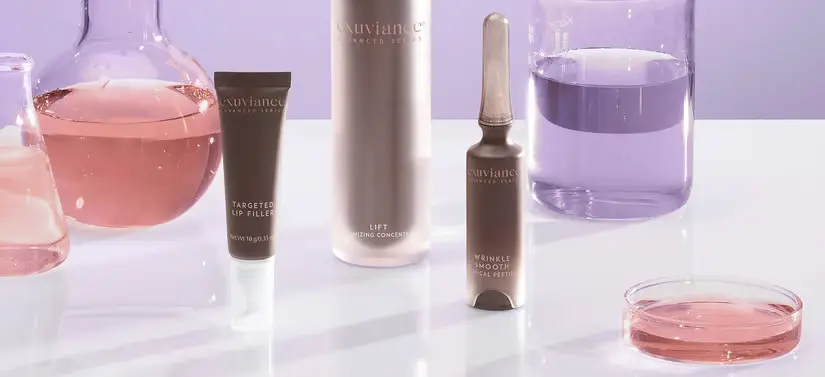 Her ses tre Exuviance produkter blandt nogle glas med farverige væsker. Baggrunden er lilla. 