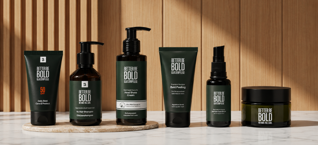 Better Be Bold glatzenplejeprodukter står opstillet på marmorbord foran en trævæg, herunder solbeskyttelse, shampoo, shave cream, peeling, serum og plejecreme til skaldet hoved.