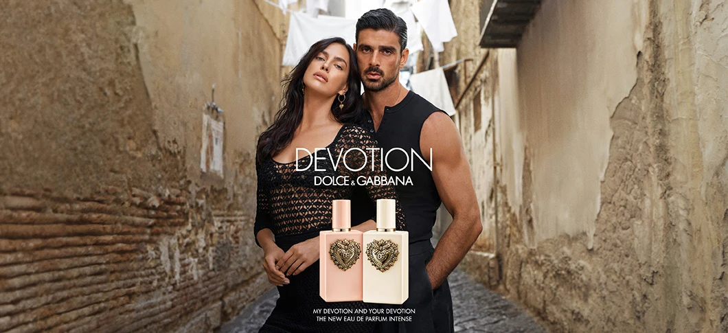 Her ses to Dolce & Gabbana Devotion-parfumeflakoner i rosa og cremefarvede nuancer med guldfarvede lågdetaljer og dekorative hjerteemblemer på forsiden. Flakonerne står ved siden af hinanden foran lyst stof..