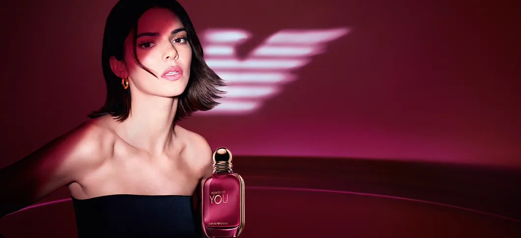 Her ses et billede med en Kendal Jenner placeret til venstre mod en rød baggrund samt en parfumeflakon til højre. På flakonen står teksten “POWER OF YOU” og “EMPORIO ARMANI”. Nederst til venstre i billedet står teksten “KENDALL JENNER”.