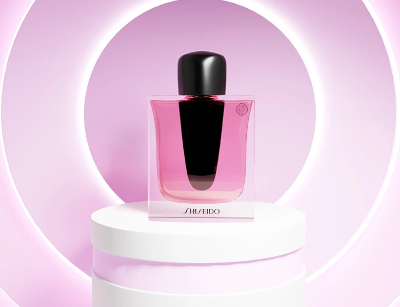 Her ses et billede af en parfumeflakon fra Shiseido placeret på et podium mod en pink baggrund med cirkulært lys. Flakonen er i pink nuance med sort låg og har teksten “SHISEIDO” nederst på flasken.