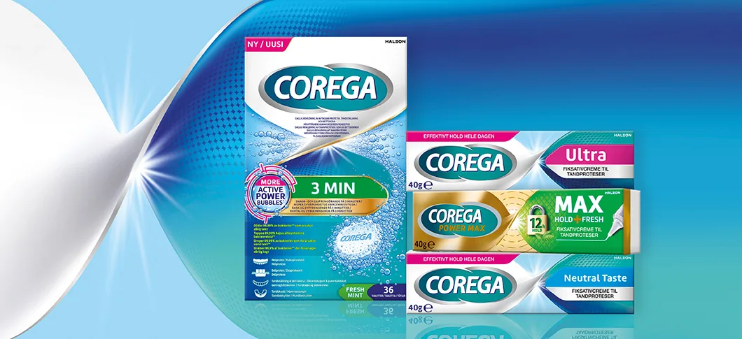 Her ses fire Corega produkter. Ét vises stående forfra i midten. De andre tre er stablet liggende med den smalle front forrest. Baggrunden er blå og hvidi