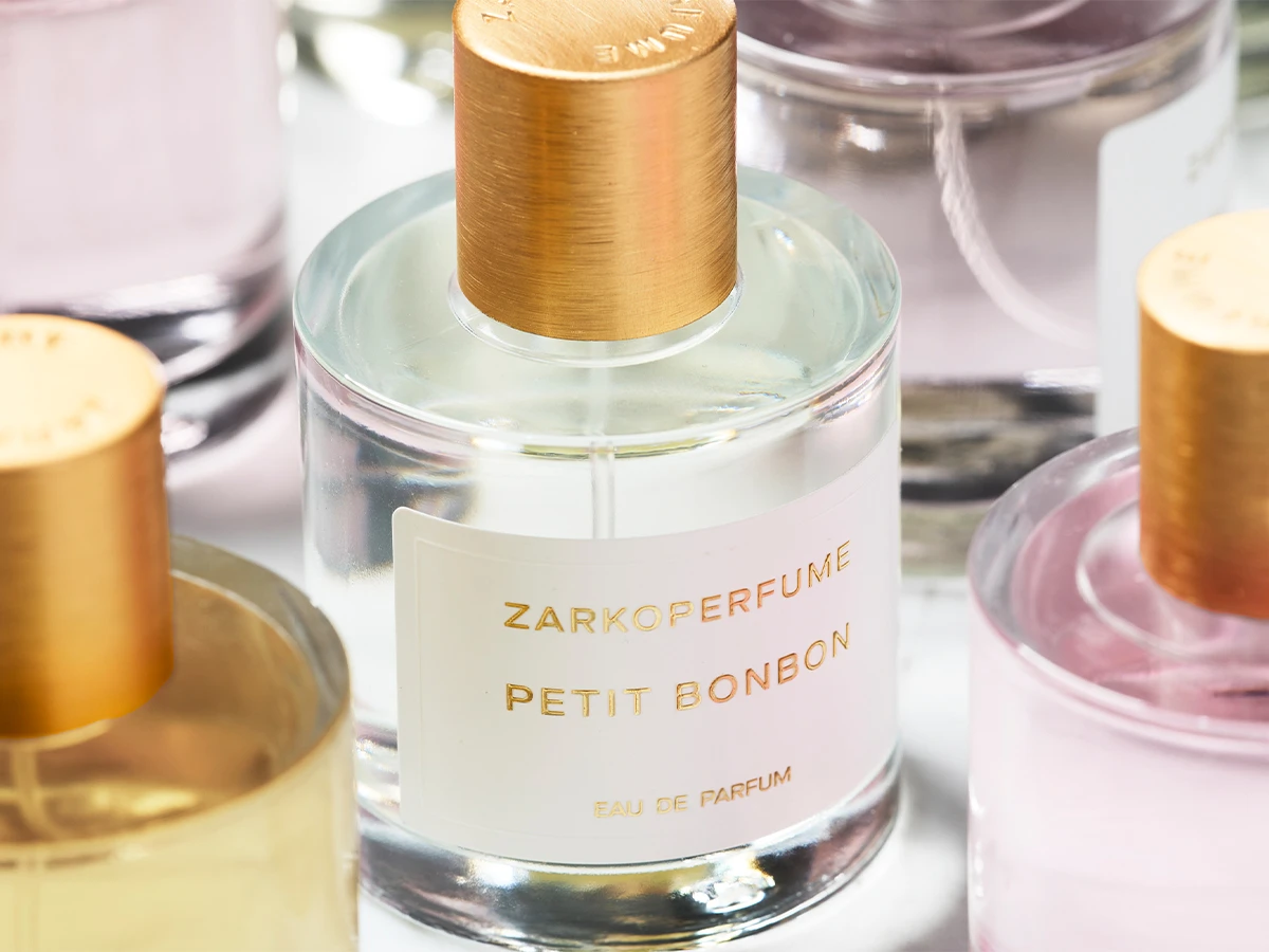 Her ses Zarkoperfume Petit Bonbon Eau de Parfum i en transparent parfumeflakon med guldfarvet låg og hvid etiket. Omkring flakonen ses andre Zarkoperfume-dufte i lyse rosa og gyldne nuancer.