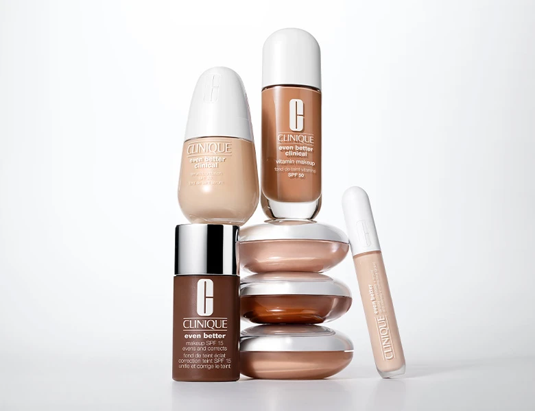 Her ses et billede med makeup-produkter fra Clinique placeret på dekorative glasformer mod en lys baggrund. Produkterne omfatter blandt andet foundation og concealer fra “Even Better”-serien.