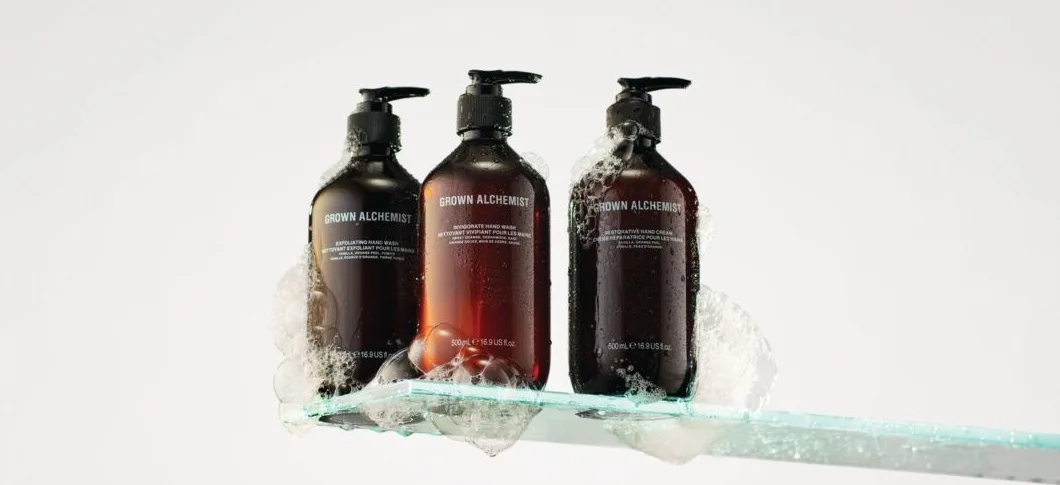 Her ses et billede med tre produkter fra Grown Alchemist placeret på en glashylde mod en lys baggrund. På produkterne står teksten “GROWN ALCHEMIST”. Produkterne er i mørke flasker med pumpe og er omgivet af skum.