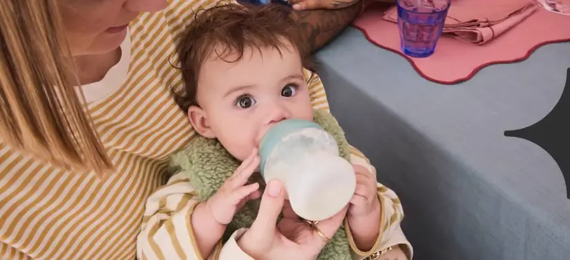 Her ses en kvinde som sidder med en baby, som drikker af en sutteflaske
