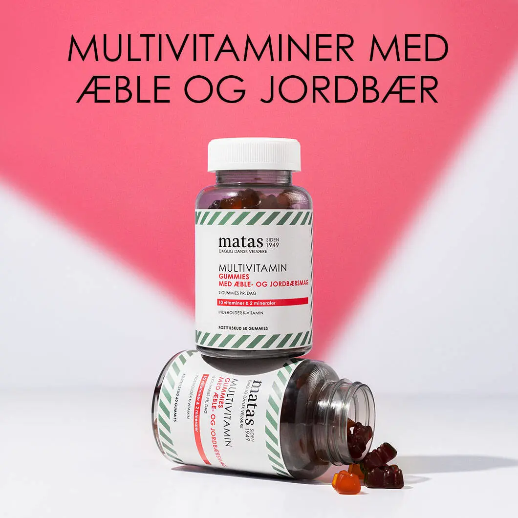 Her ses en rød og hvid baggrund med en sort tekst øverst. Under ses to bøtter af Matas vitaminvingummier med æble- og jordbærsmag. Den ene bøtte er liggende og åben, hvor der er nogle enkelte vingummier på vej ud.