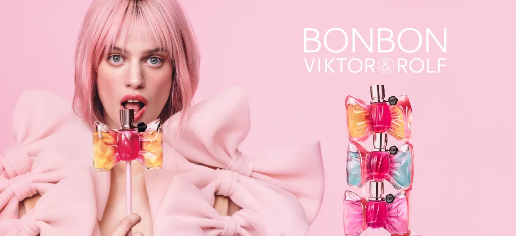 Her ses et billede af en person med lyserødt hår mod en lyserød baggrund, der holder en parfumeflakon formet som en sløjfe. Til højre står teksten “BONBON VIKTOR&ROLF”. Der ses tre Bonbon-parfumeflakoner i forskellige farver stablet oven på hinanden.