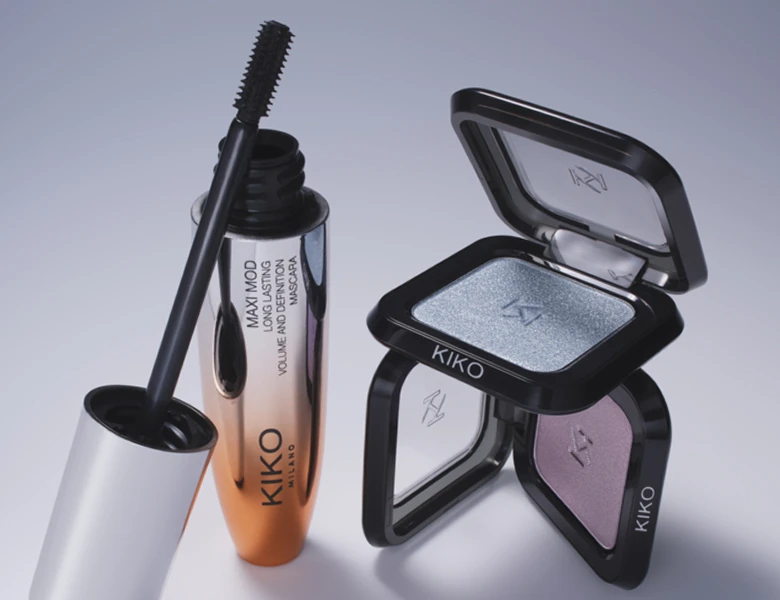 Her ses et billede med øjenmakeup-produkter fra KIKO Milano placeret mod en lys baggrund. Der ses blandt andet mascara og øjenskygger, og på produkterne står tekster som “MAXI MOD Long Lasting Mascara”. Produkterne er i sorte, gyldne og metalliske nuancer.
