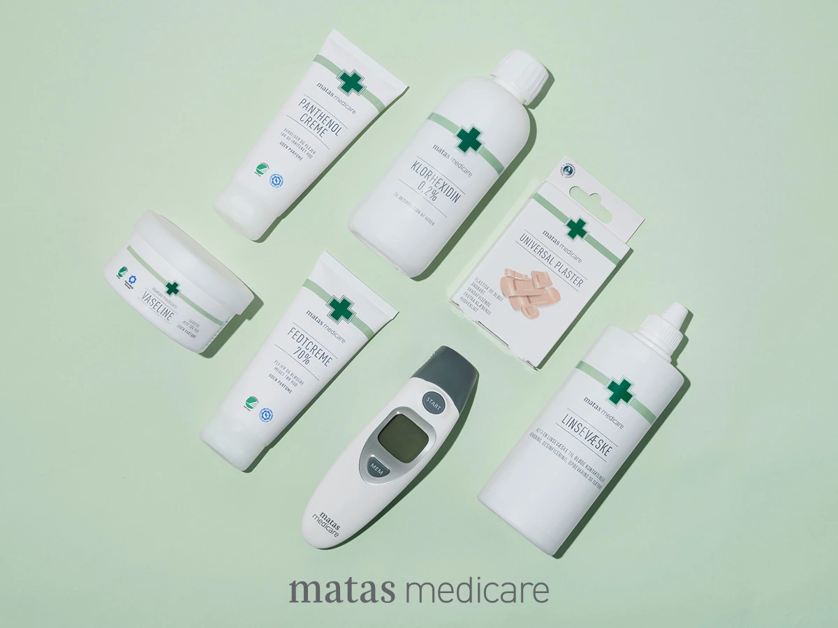 En samling af Matas Medicare produkter: Panthenol Creme, Vaseline, Fedtcreme, Klorhexidin, Universal Plaster, Linsevæske og et termometer.