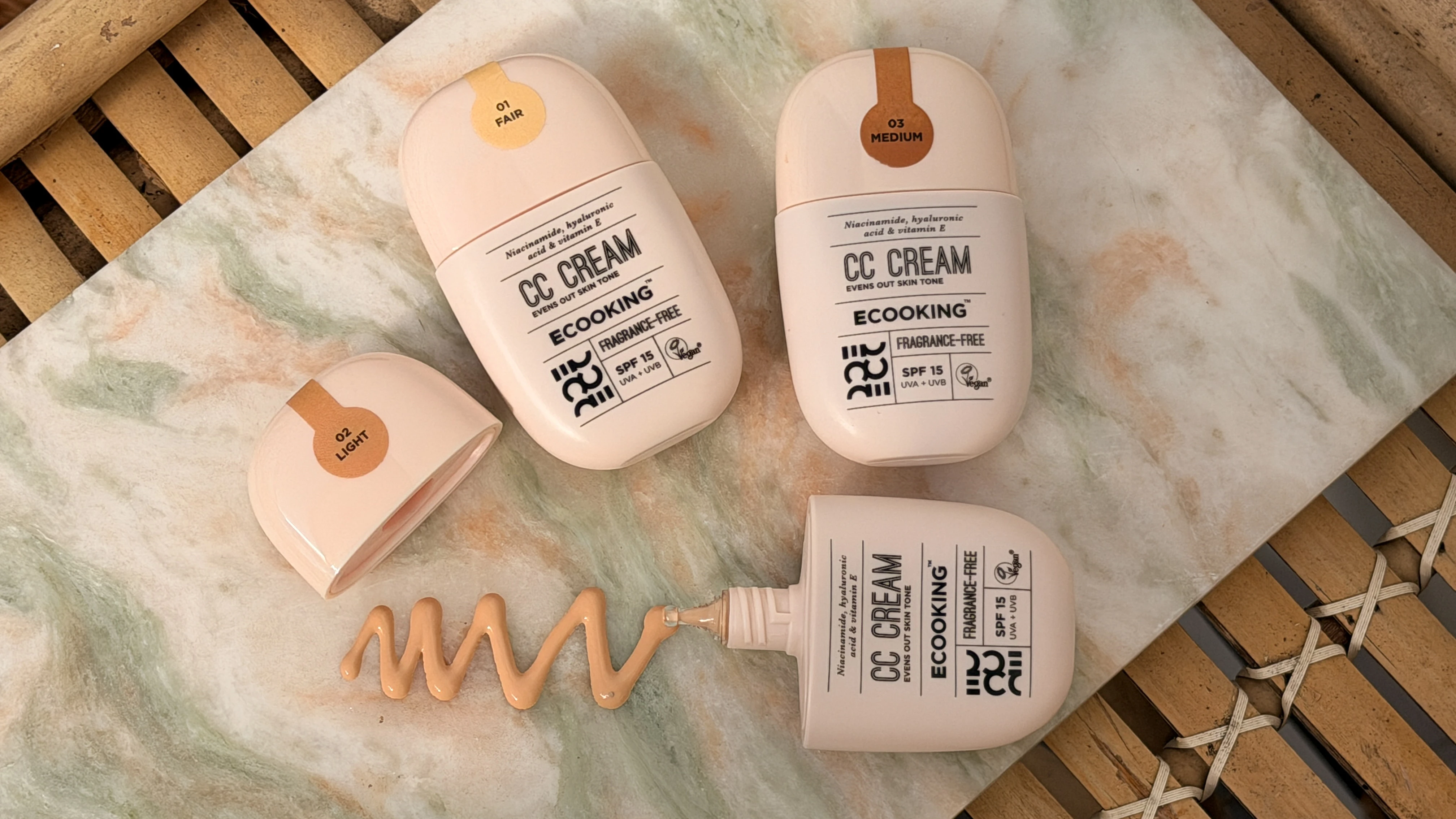 Tre flasker Ecooking CC Cream i nuancerne 01 Fair, 02 Light og 03 Medium, med en klat creme presset ud.