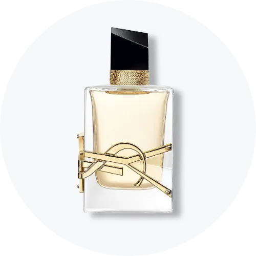Her ses en parfumeflakon fra Yves Saint Laurent med lyst gyldent indhold, sort låg og guldfarvede detaljer. Det ikoniske YSL-logo pryder forsiden af den transparente flakon, som står centralt mod en lys, rund baggrund.