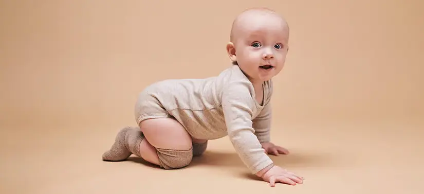 Her ses en beige baggrund med en glad kravlende baby, som kigger lige ind i kameraet. 