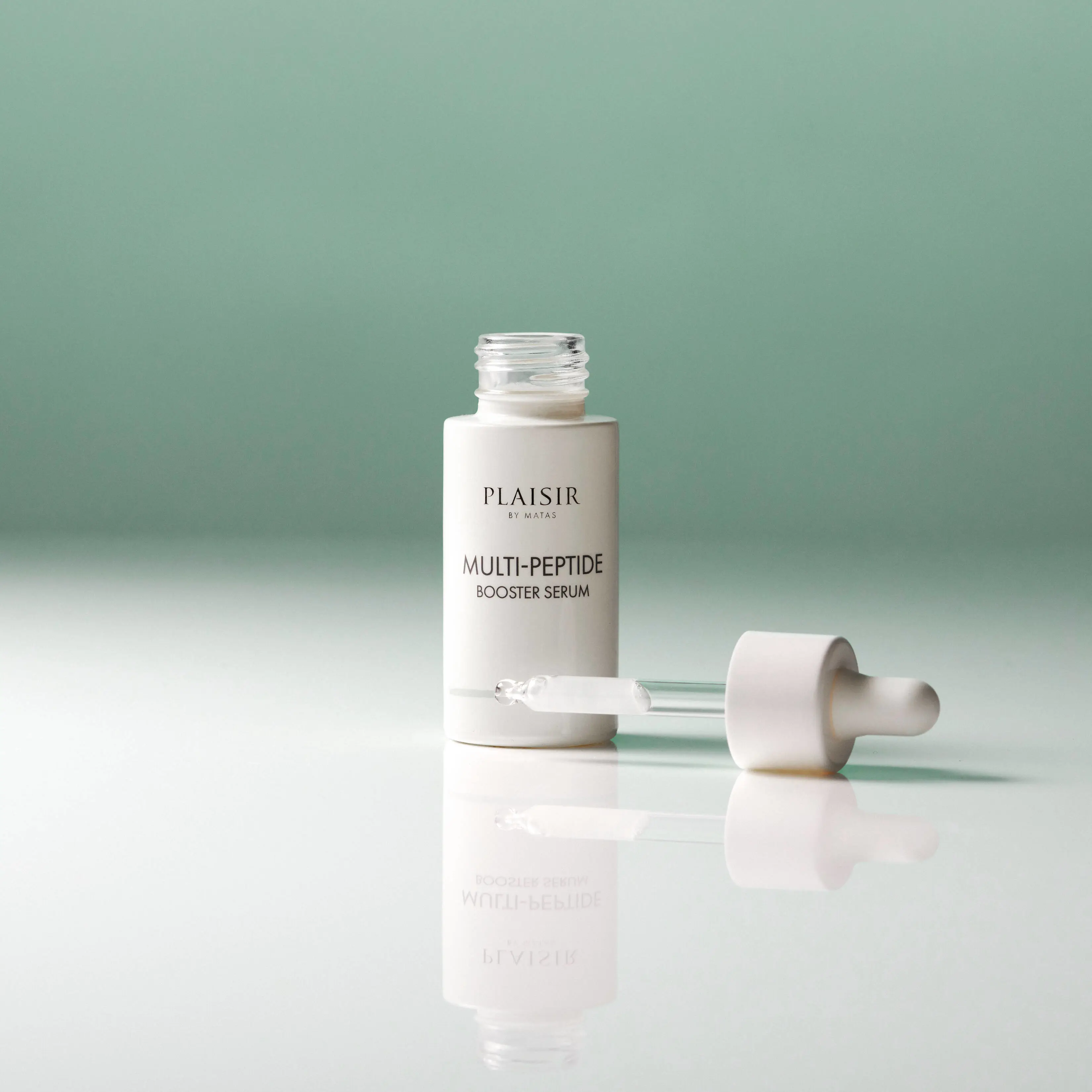 En flaske Plaisir Multi-Peptide Booster Serum står åben på en blank overflade mod en grøn baggrund. Pipetten ligger ved siden af med en dråbe serum i spidsen. Flasken spejler sig i underlaget.