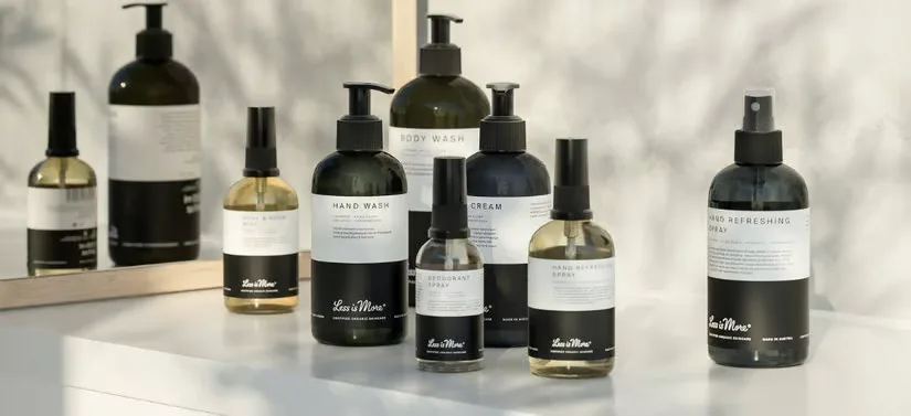Her ses en masse produkter fra Less Is More stående på et lyst badeværelsesbord. Selve produkterne er mørke med hvide labels.