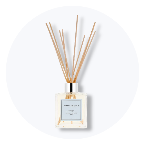 Firkantet glasflaske med sølvhætte og brune pinde, der fungerer som en duftspreder. På flaskens blå etiket står 'TREMORORG deluxe aroma therapy'.