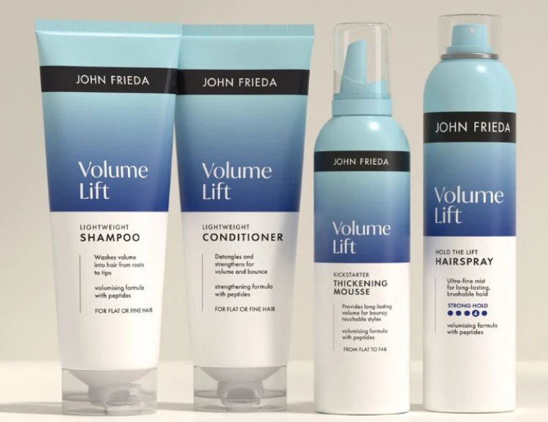Her ses et billede med hårplejeprodukter fra John Frieda placeret mod en lys baggrund. På produkterne står teksten “Volume Lift”, og serien indeholder blandt andet shampoo, conditioner, mousse og hårspray. Nederst står teksten “VOLUME”.