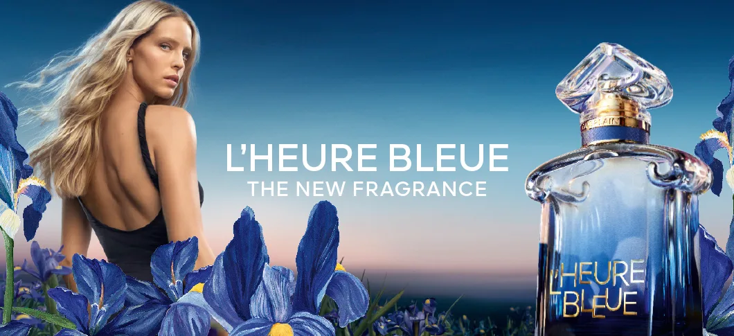 Her ses et kampagnebillede for Guerlain L’Heure Bleue. Til venstre ses en person med langt lyst hår i sort tøj omgivet af blå irisblomster, og til højre ses den blå parfumeflakon. I midten står teksten “L’Heure Bleue – The New Fragrance”.