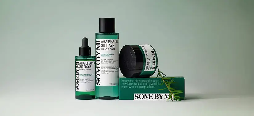 Her ses tre grønne SOME BY MI produkter, hvoraf et af dem ligger på en SOME BY MI æske. Ved siden er der en gren og baggrunden er grøn.