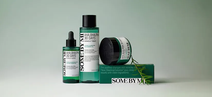 Her ses tre grønne SOME BY MI produkter, hvoraf et af dem ligger på en SOME BY MI æske. Ved siden er der en gren og baggrunden er grøn.