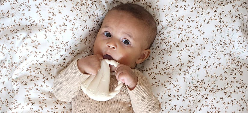Baby ligger på blomstret tæppe og bider i en lys silikonebidering.
