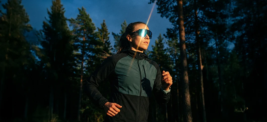 Kvinde løber i en skov ved lavt sollys og har store sportsbriller på samt mørkt løbetøj fra Ortho Movement