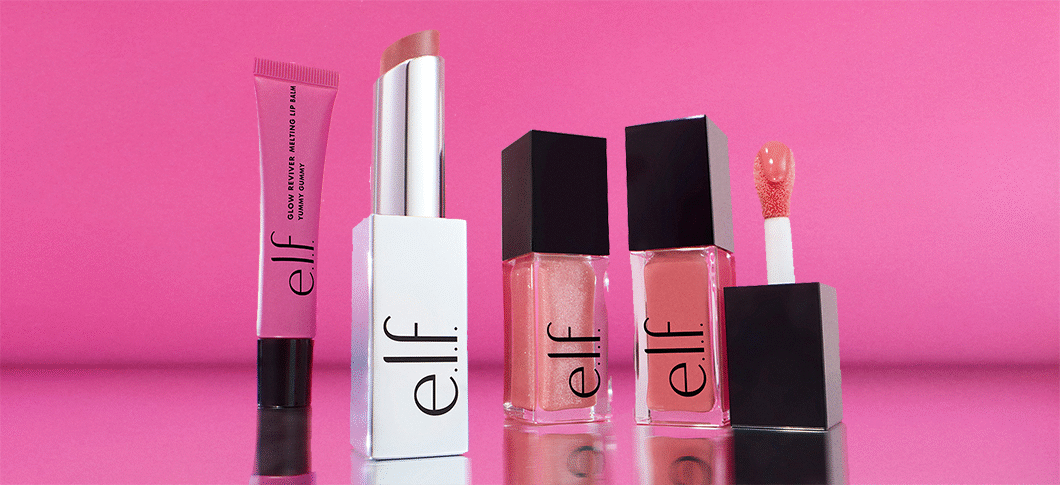Her ses en pink baggrund med forskellige elf produkter; en lip balm, en læbestift og to lip oils.
