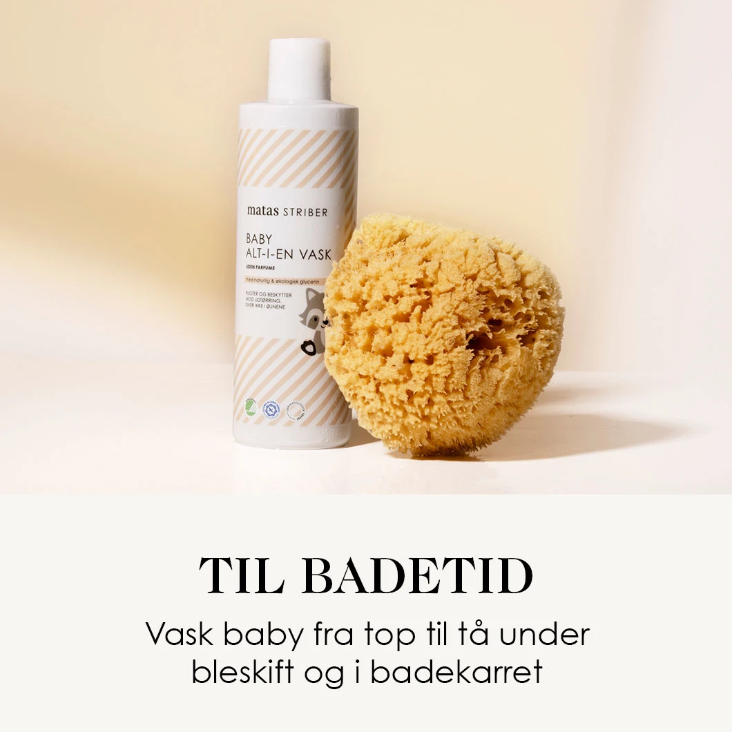 Her ses en baby alt-i-en vask og en svamp på en lys baggrund. Under ses en sort tekst på en hvid baggrund. 