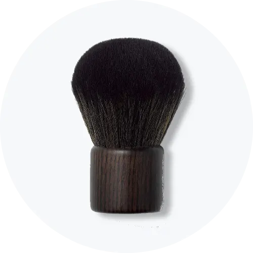 Her ses et billede af en makeupbørste fra Nilens Jord placeret centralt mod en lys baggrund. Børsten har mørke børstehår og et kort, mørkt skaft.