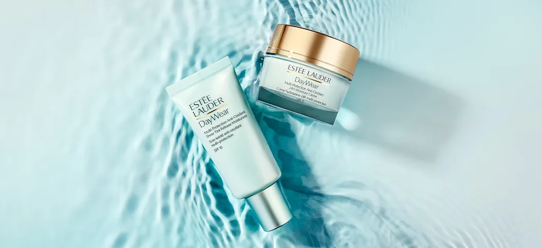 Her ses et billede med hudplejeprodukter fra Estée Lauder placeret over en vandinspireret baggrund. På produkterne står teksten “DayWear”, og emballagen er i lyseblå og gyldne nuancer.