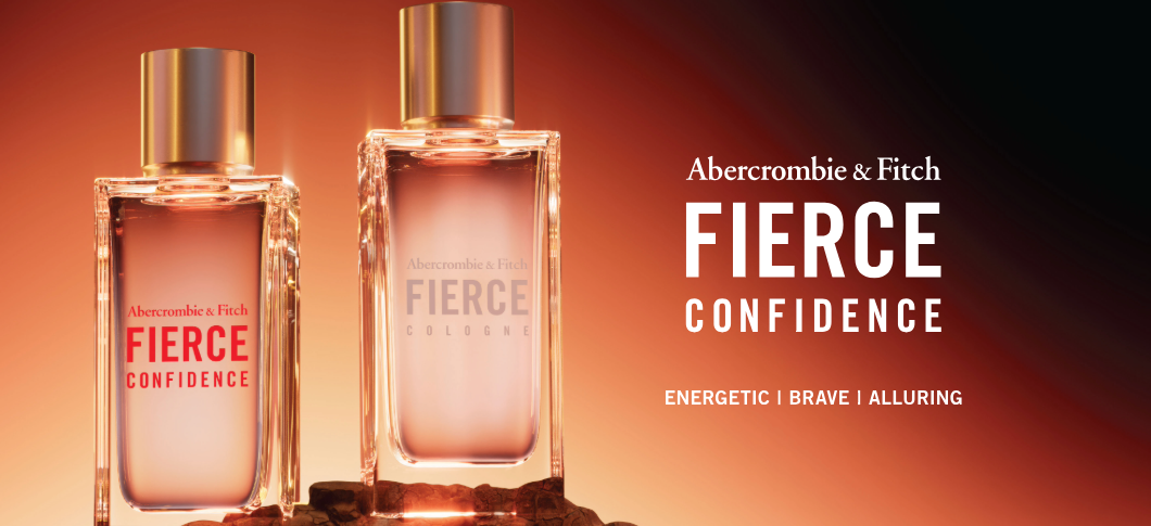 Her ses et billede med to parfumeflakoner fra Abercrombie & Fitch placeret på en klippeagtig overflade mod en varm orange baggrund. På billedet står teksten “Abercrombie & Fitch FIERCE CONFIDENCE” samt “ENERGETIC | BRAVE | ALLURING”. Flakonerne har guldfarvede låg og transparente glasflasker i varme nuancer.