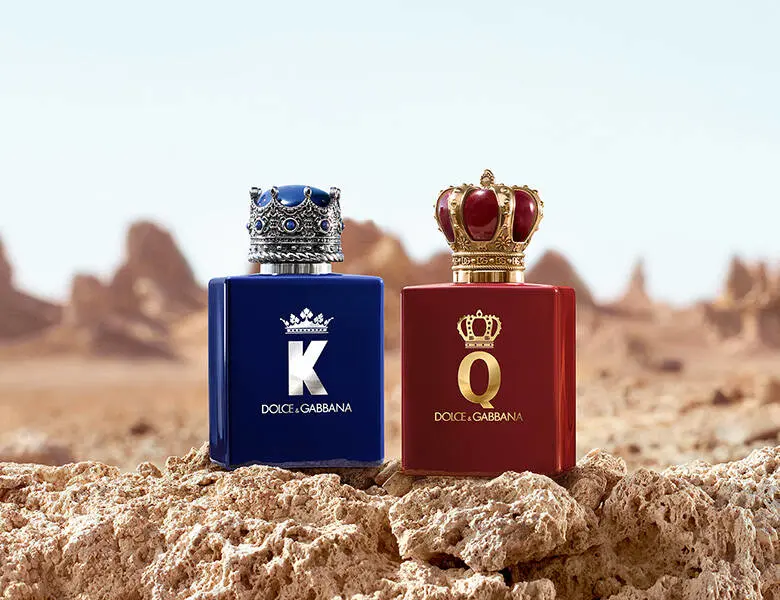 Dolce & Gabbana K og Q parfumer i blå og rød flaske med kronelåg står på klipper i et tørt ørkenlandskab