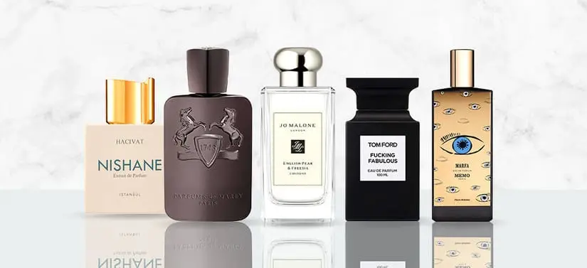 Her ses et billede med flere parfumeflakoner fra forskellige brands placeret side om side mod en lys, marmorlignende baggrund. På flakonerne står blandt andet “NISHANE”, “PARFUMS DE MARLY”, “JO MALONE”, “TOM FORD” og “MEMO”. Flakonerne har forskellige former og farver.